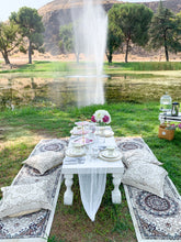Load image into Gallery viewer, Picnic setup outdoors at a park with pillows, picnic table, china plating, silverware and a beverage station for hot tea and sparkling beverages